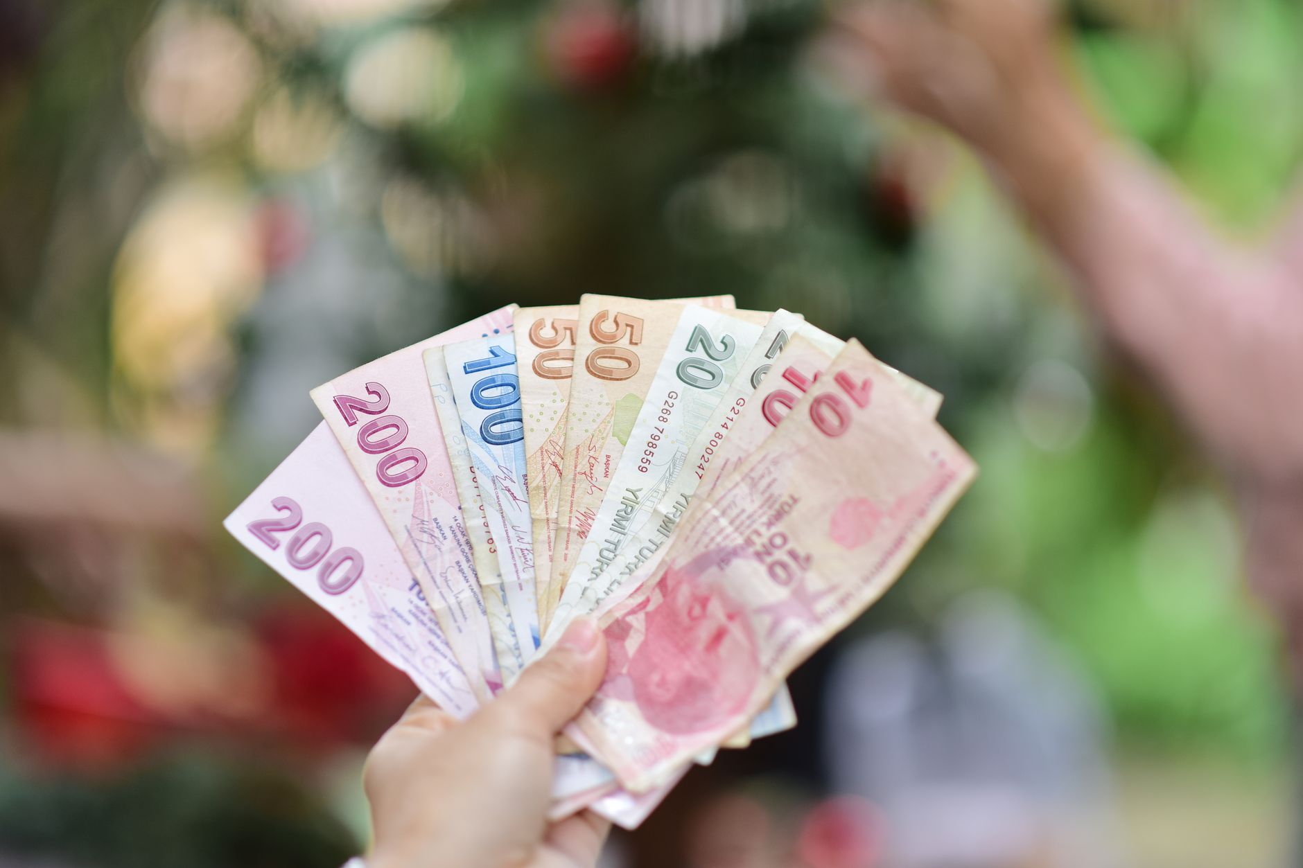 A hand holding multiple Turkish Lira banknotes in an outdoor setting, showcasing various denominations. — Casino Sites Review