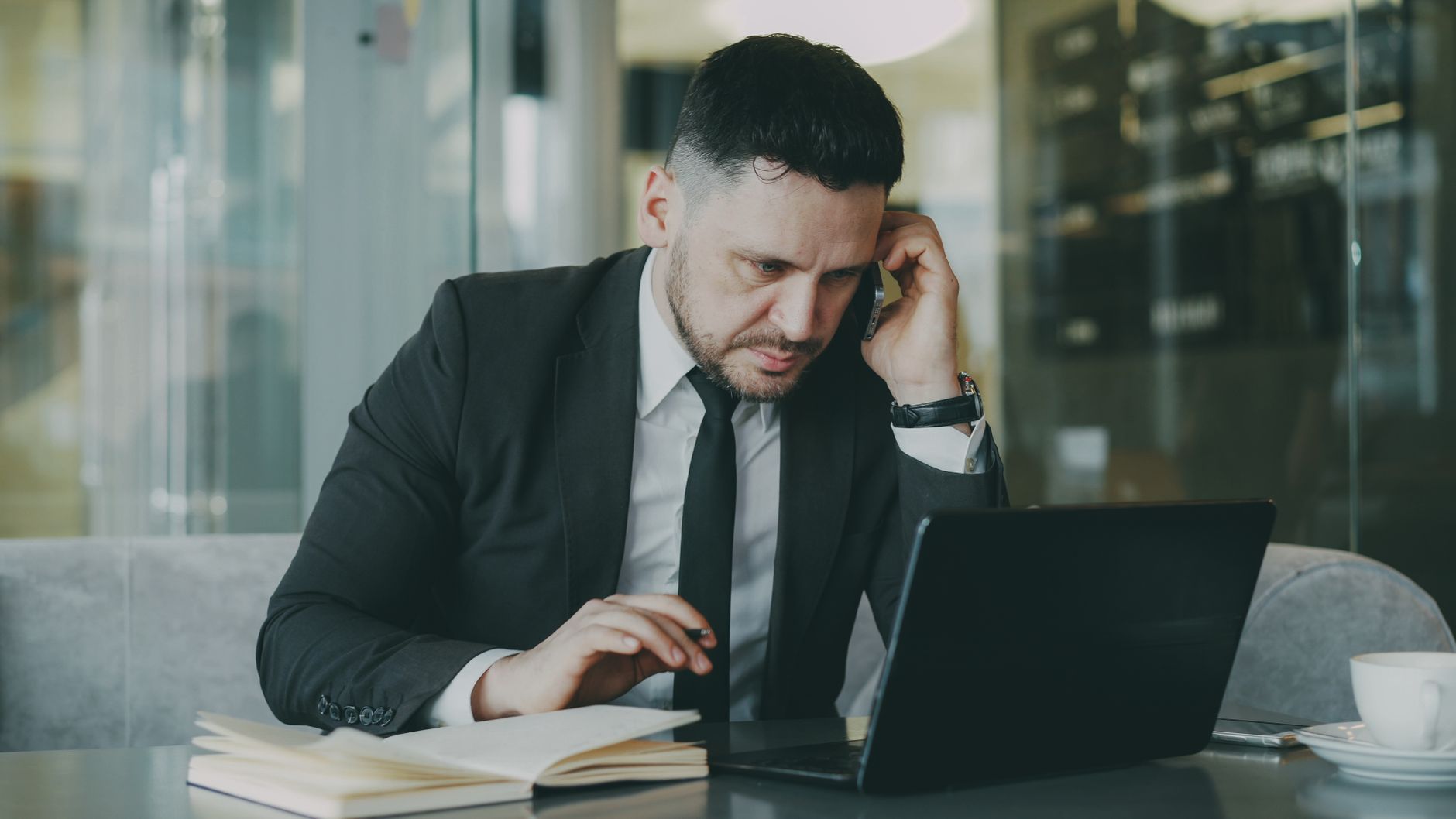 Focused businessman in suit multitasking on phone and laptop in modern office. — Effortless Hosting Through Airbnb Solutions
