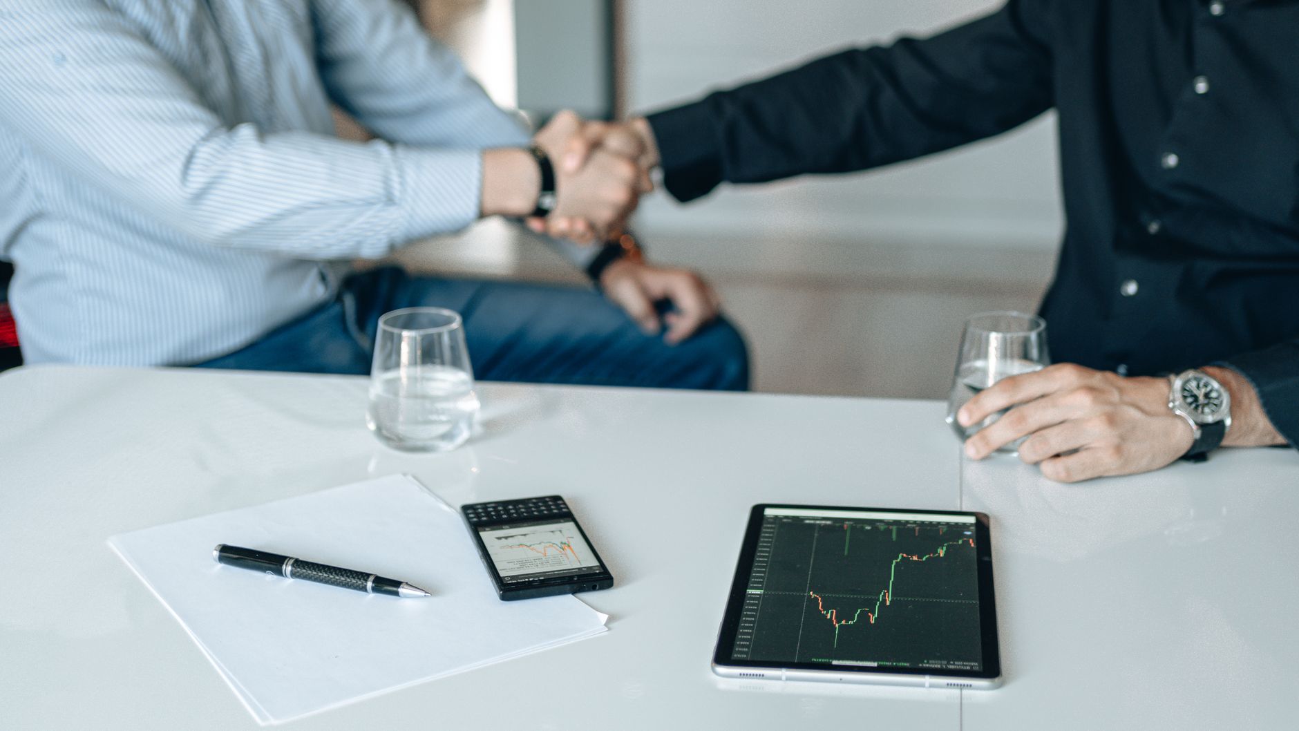 Business meeting with handshake and financial analysis displayed on a tablet. — The Vital Role of Valvular Surgery: Rediscove